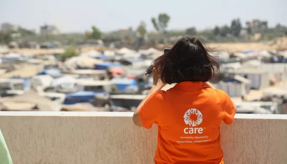 Back of woman wearing orange t-shirt with CARE's logo looking at a blurry site of an outdoor area