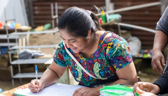 Woman wearing patterned t-shirt writing on notebook.