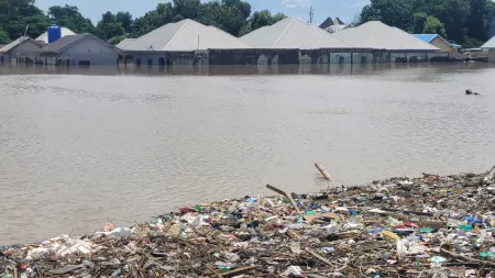 Flooded homes with water reaching halfway up the walls. The foreground shows a large pile of debris and trash.