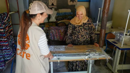 A CARE Maroc team member assists a smiling woman in a headscarf as they unwrap a knitting machine in a community workspace. 