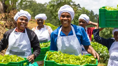 women carrying tea lives, smiling, wearing white caps and aprons