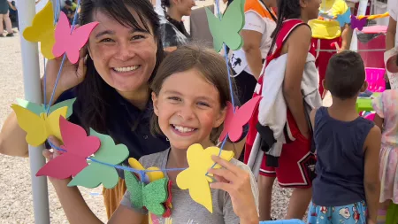 Girl with brown hair and woman behind her with dark her similing while holding rope with colorful rubber butterflies.