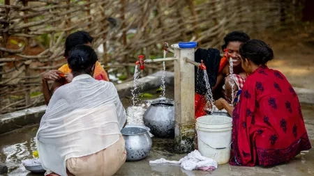 Women sitting on the floor filling buckets with tap water