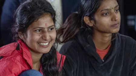 Girl sitting on the floor smiling, with the profile of the another girl sitting next to her