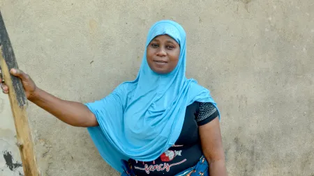 Woman wearing blue scarf standing against wall, smiling softly at the camera