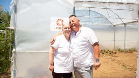 Elderly woman and man hugging and smiling athe camera in front of a greenhouse. t of a 