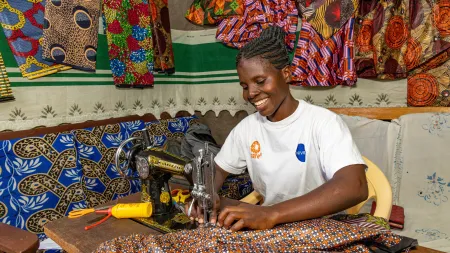Mildred works at her sewing machine, using skills and support to build a stable income and support her family.