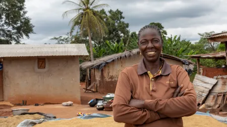 Woman standing in front of a wide deposit of grains. The woman weaes brown clothes, has her arms crossed and is smiling to the camera.