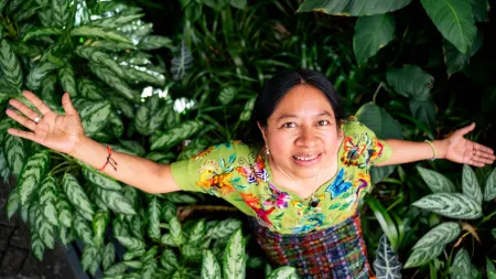 Woman wearing patterned dress standing in a plantation while looking up at the camera.