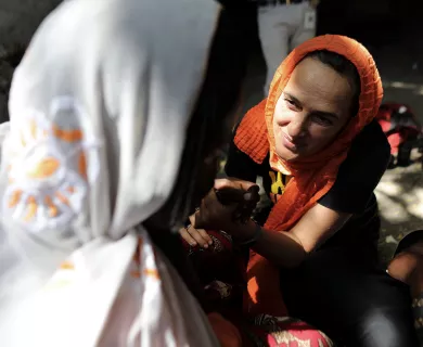 CARE International Secretary General Sofia Sprechmann, wearing an orange head scarf, clasps the hand of a woman, whose face is not visible.
