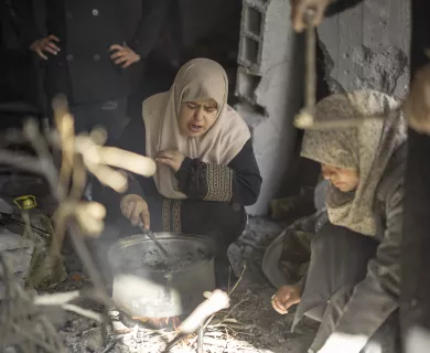 Two women in hijabs cooks over a makeshift fire in a damaged building in Gaza.