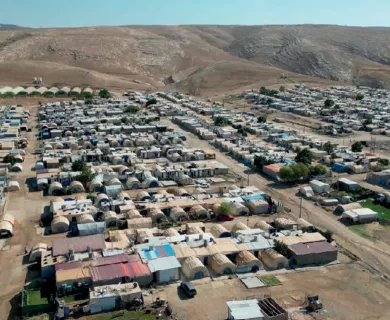 An aerial view of a sprawling refugee camp with numerous tents and makeshift shelters nestled in a arid, mountainous landscape.