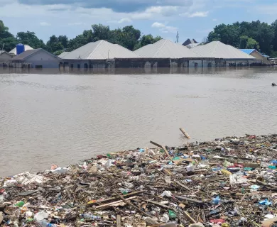 Flooded homes with water reaching halfway up the walls. The foreground shows a large pile of debris and trash.