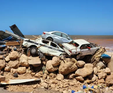 A pile of wrecked cars and debris stacked on a rocky shoreline, remnants of destruction caused by severe flooding in Libya.