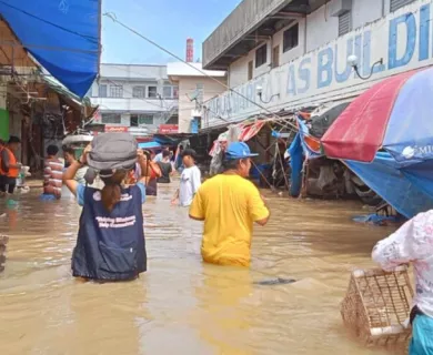 People wade through flood waters at a market in the Philippines, with vendors and customers navigating waist-deep brown water.