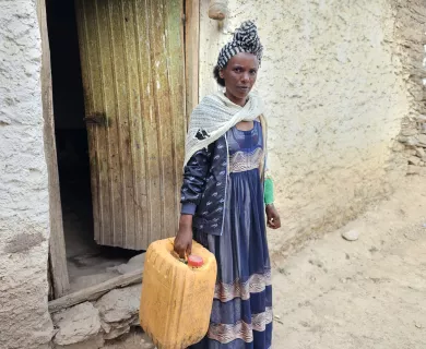 Woman with blue dress holding a jerry can in front of a door