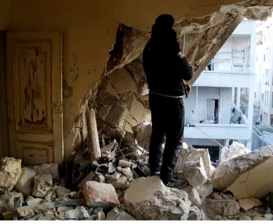 Person standing amid rubble and looking at destroyed wall