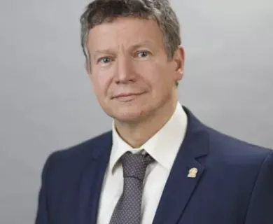 Portrait of man with short hair and light eyes, wearing blue suit,white short and grey tie 
