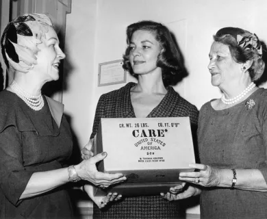 Black and white photo of three women holding the CARE package in the 1950s.