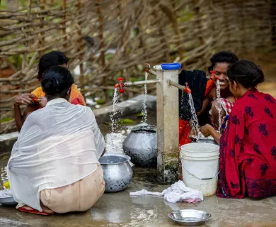 Women sitting on the floor filling buckets with water coming from taps
